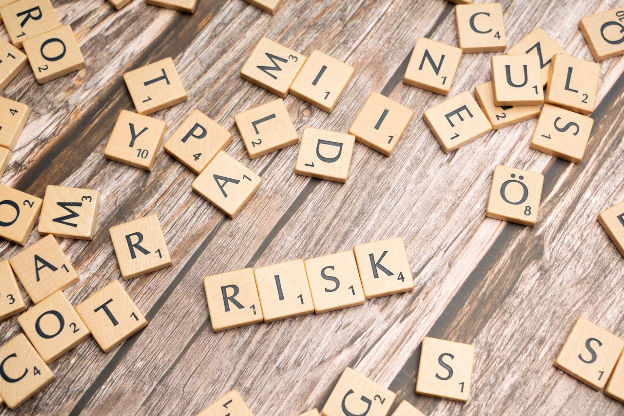 services-02 Scrabble tiles spelling out 'risk' scattered on a rustic wooden background, symbolizing uncertainty.